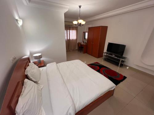 a bedroom with a white bed and a television at Hotel La Roche in Brazzaville
