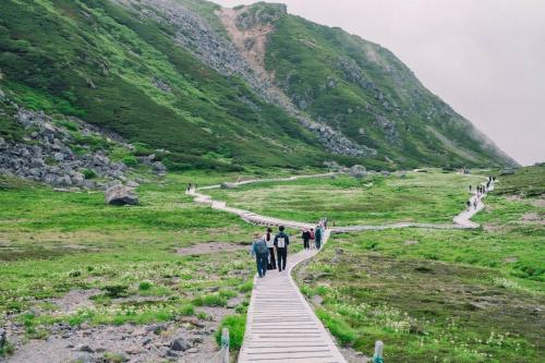 a group of people walking on a wooden path through a mountain at Raicho Onsen Inn in Matsumoto