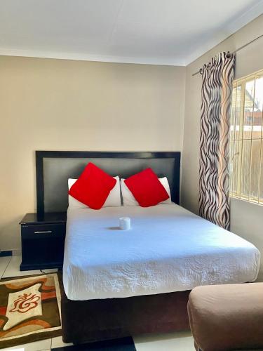 a bedroom with a bed with red pillows and a window at Miraton Eastgate Suites in Johannesburg