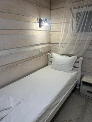 a white bed in a room with a wooden wall at Купецький Двір in Mizhhirʼʼya