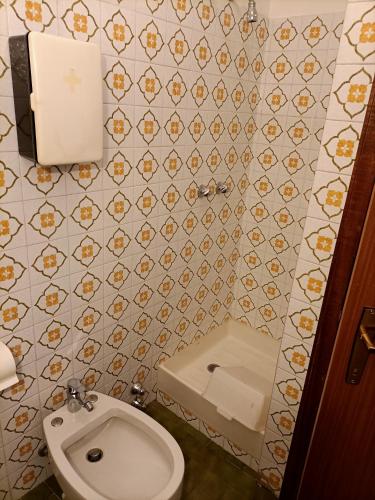 a bathroom with a toilet and a tiled wall at Appartamenti Alpino in Baselga di Pinè
