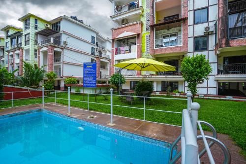 a swimming pool with an umbrella and some buildings at Skylight BnB F203 - 2BHK with pool near Candolim beach in Candolim