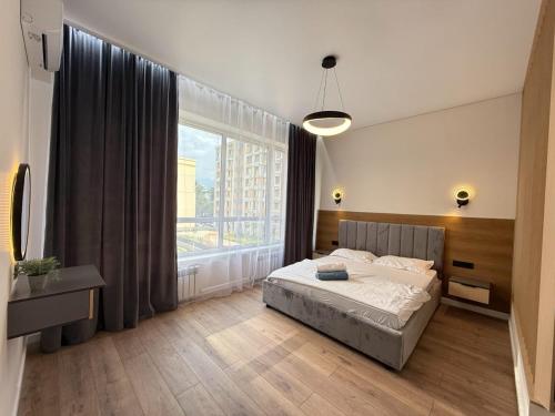 a bedroom with a bed and a large window at Уютная в центре города in Zhezdi