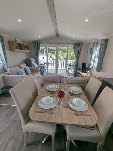 a wooden table with plates and glasses on it in a living room at Modern Spacious Willerby Malton Caravan at Durdle Door Holiday Park, Close to Iconic Durdle Door & Lulworth Cove in West Lulworth