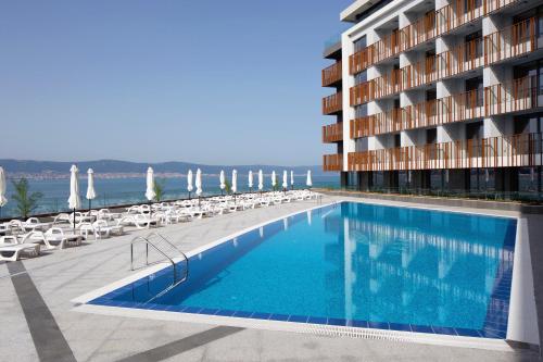 a swimming pool in front of a building with chairs at Aparthotel Paradiso in Nesebar