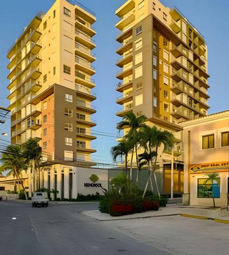 two tall buildings with palm trees in front of a street at Caribbean Sunset Soak In Juan Dolio Beach Apt. in Juan Dolio