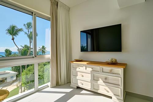 a living room with a tv and a large window at Caribbean Sunscape Beachfront Apartment in La Puntica de Juan Dolio