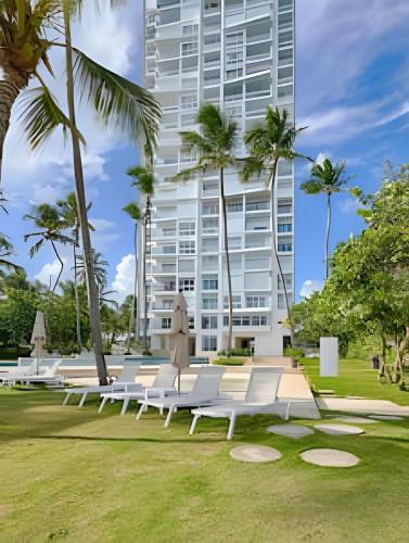 a row of white benches in a park with a tall building at Caribbean Sunscape Beachfront Apartment in La Puntica de Juan Dolio