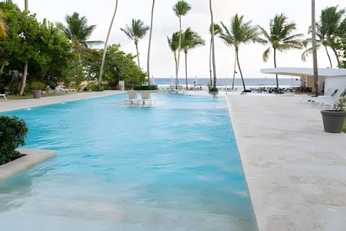 a pool at a resort with palm trees and the ocean at Caribbean Sunscape Beachfront Apartment in La Puntica de Juan Dolio