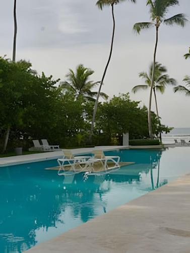a swimming pool with two chairs and palm trees at Caribbean Sunscape Beachfront Apartment in La Puntica de Juan Dolio