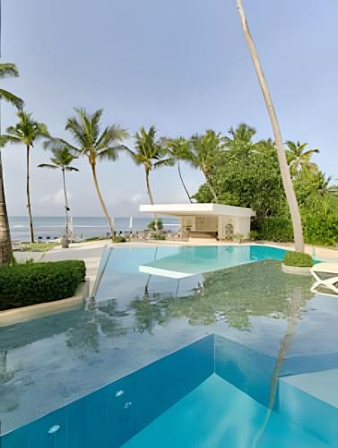 a swimming pool with palm trees and the ocean at Caribbean Sunscape Beachfront Apartment in La Puntica de Juan Dolio