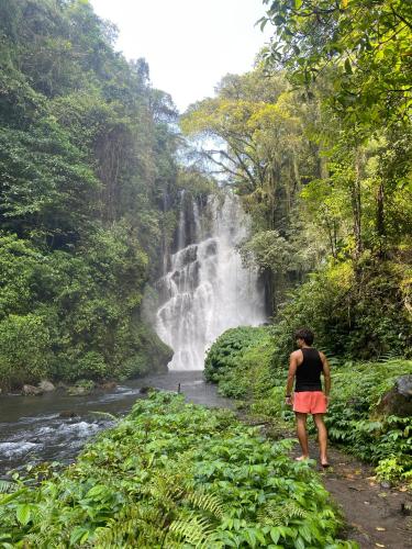 a woman walking down a path in front of a waterfall at Tranquil Riverside Camping in Ambengan
