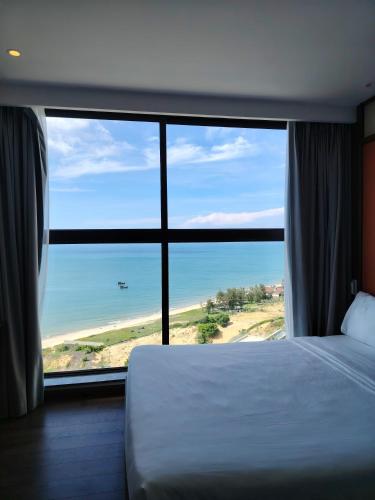 a bedroom with a large window with a view of the beach at Apec Mandala wyndham Apartment - APEC Mui Ne in Mui Ne
