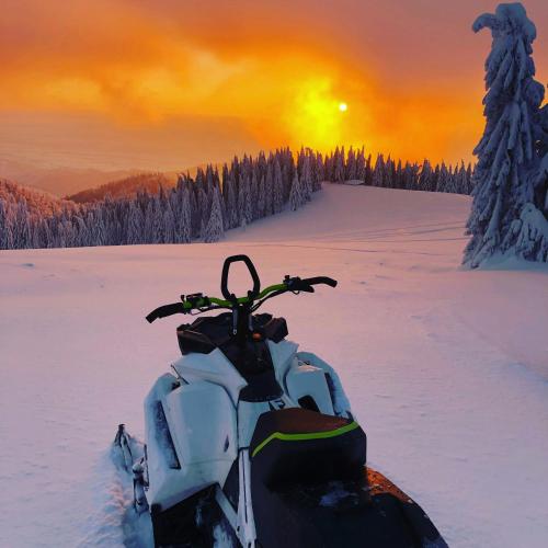 a snowmobile parked in the snow with the sunset at Serenity Levi - Hot Tub & Sauna in Levi