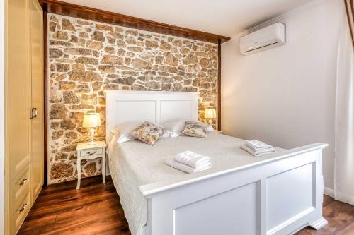 Cama blanca en habitación con pared de piedra en Villa Frana, en Krk
