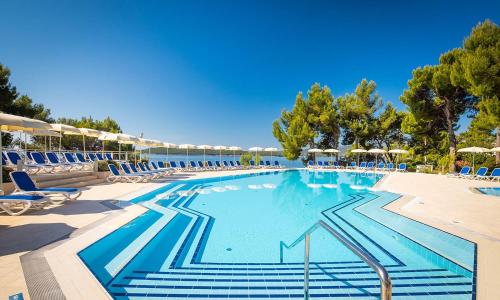 a large swimming pool with blue chairs and water at Aminess Vival Grand Azur Hotel in Orebić