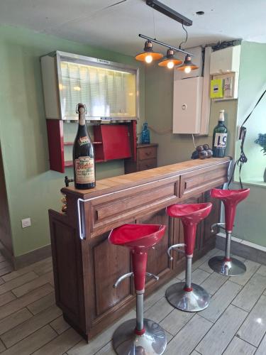 a bar with a bottle of wine and red stools at Maison spacieuse et calme in Bayonville