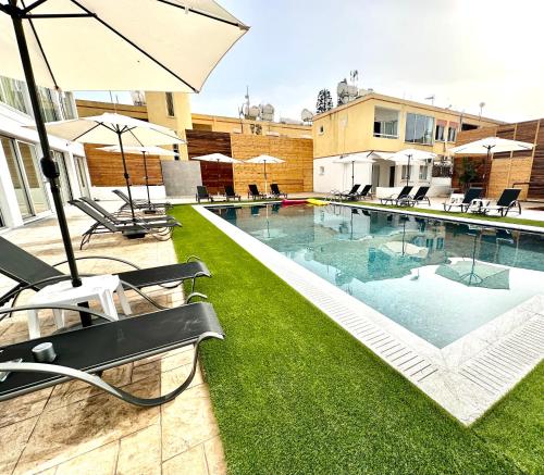 a swimming pool with lawn chairs and an umbrella at Sun Plaza Suites - Adults Only in Ayia Napa