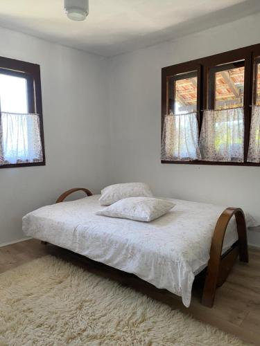 a white bedroom with a bed with two windows at Organska Farma Nebesa in Vrmdža