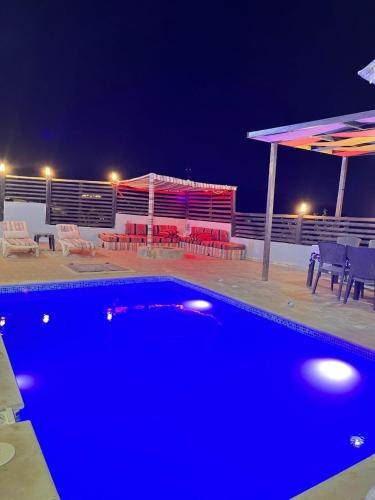 a blue swimming pool at night with chairs and umbrellas at شاليه بانا جرش in Jerash