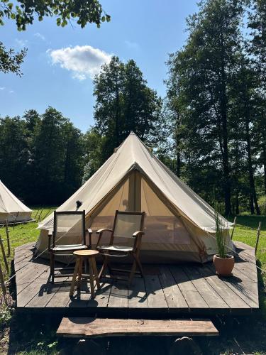 a tent with two chairs and a table in front of it at Glamp Juodis in Ubiškės