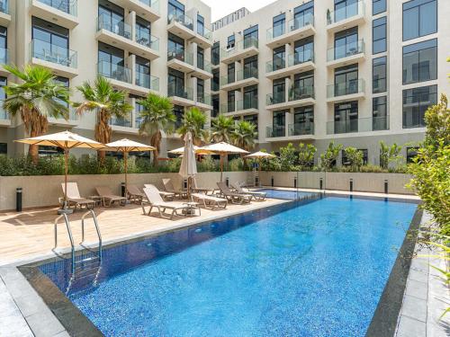 a swimming pool with chairs and umbrellas in front of a building at Savis Homes - Luxury Brand New Studio in Elysee III in JVC in Dubai