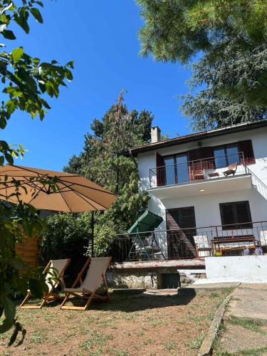 a house with chairs and an umbrella in front of it at Kućica na brdu-Zaklopača in Zaklopača