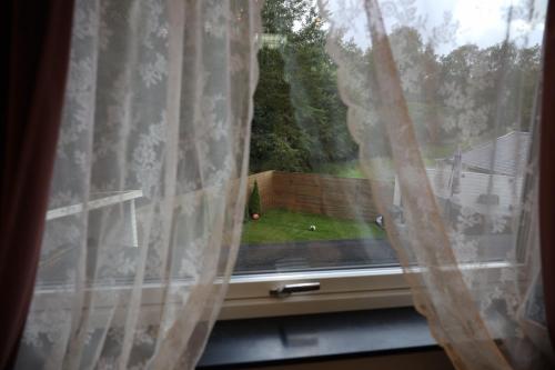 a window with white curtains and a view of a yard at Between the Trees in Gothenburg