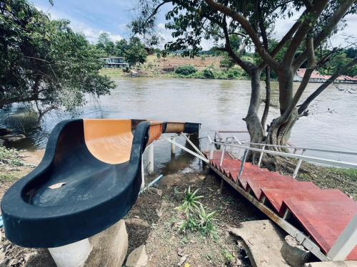 a bench sitting next to a tree next to a river at The Villa Sai yok noi in Khlong Luang