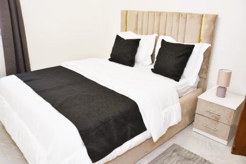a bedroom with a bed with white sheets and black pillows at Cosy by dalyda in Yaoundé