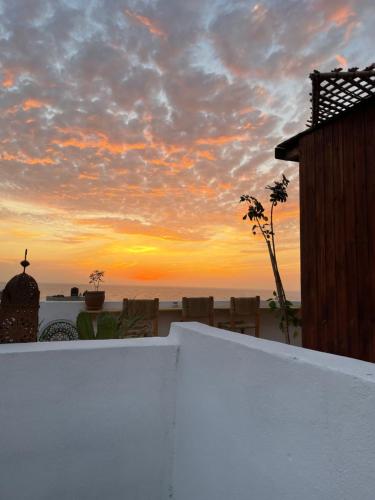a sunset over the beach with a white wall and chairs at Imsouane soul lodge in Imsouane