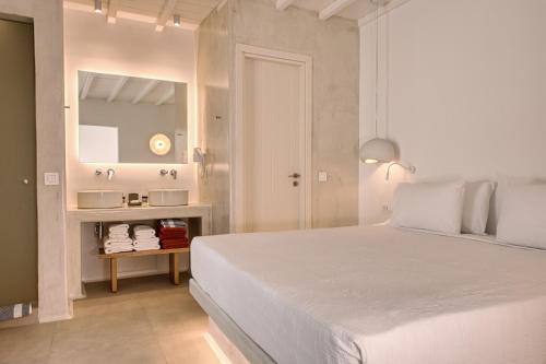 a white bedroom with a bed and a mirror at Paolas Sunset in Agios Stefanos