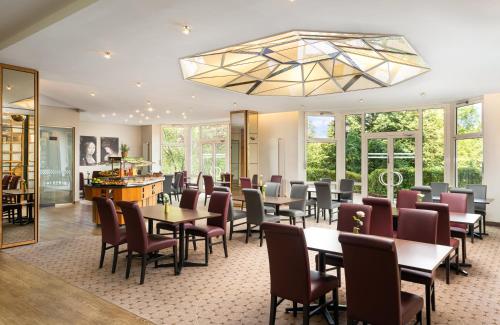a restaurant with tables and chairs and a chandelier at Leonardo Hotel Weimar in Weimar