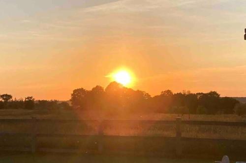 a sunset over a field with a fence and trees at Farmhouse Resort in Midhurst