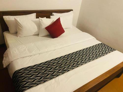 a bed with white sheets and a red pillow at New Cherry Wood Bangalow in Bandarawela