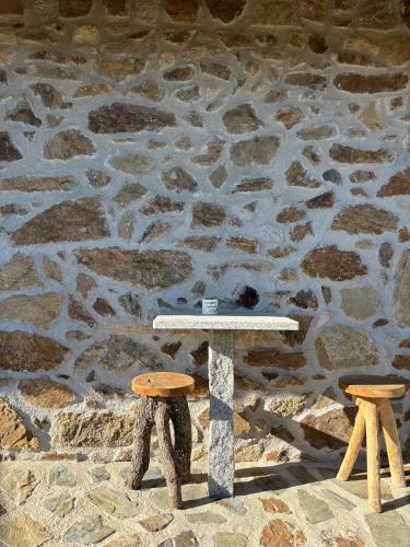 a table and two stools in front of a stone wall at Quinta Cabeço do Barragão in Fundão