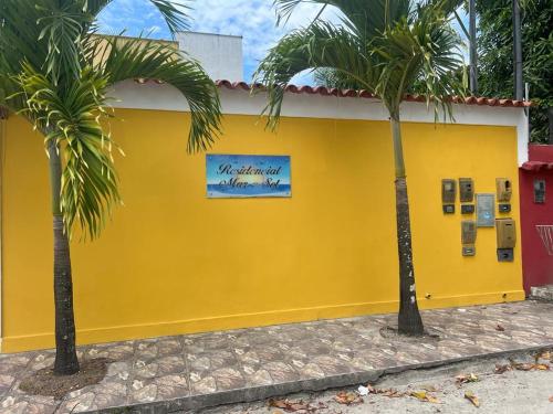 a yellow building with palm trees in front of it at Paraíso Tropical em Porto Seguro in Porto Seguro