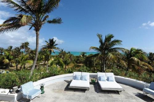a patio with chairs and palm trees and the ocean at Windsong home in South Palmetto Point