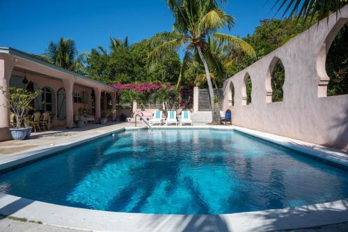 a swimming pool next to a house with a palm tree at Indigo 2BR home in Governorʼs Harbour
