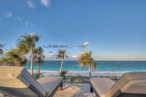 a beach with two chairs and palm trees and the ocean at Wild Orchid 3 Bedroom home in North Palmetto Point
