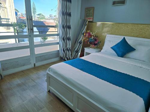 a bedroom with a bed with blue pillows and a window at HUY HOANG II Hotel - Da Lat in Da Lat