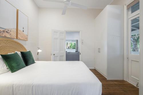 a white bedroom with a large white bed with green pillows at Cove Quarters in Byron Bay
