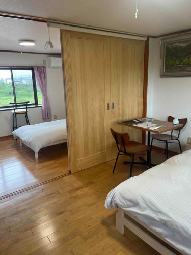 a bedroom with two beds and a desk and a table at 朝食夕食付きで最高ランクの飛騨牛希少部位と地元野菜の炭火焼きを堪能できる宿ゲストハウスつぐや in Kurono