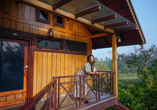 a woman standing on the balcony of a house at Niyatma Wayanad Pool Resort by VOYE HOMES in Wayanad