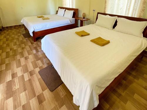 a bedroom with two beds with white sheets and wooden floors at Village House in Phong Nha