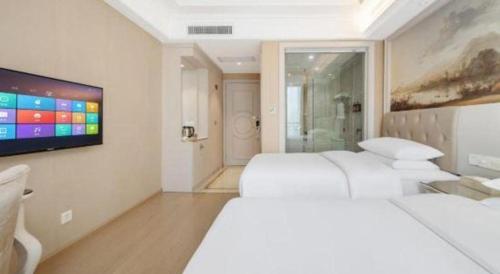 a white bedroom with two beds and a flat screen tv at Vienna Hotel Guiyang Jiaxiulou Jichang Road in Guiyang