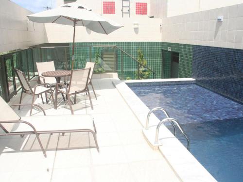 - une piscine avec des chaises, une table et un parasol dans l'établissement Apartamento Praia Jatiúca, à Maceió