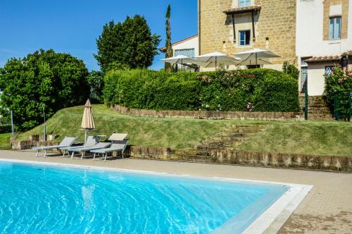 a swimming pool with chairs and an umbrella next to a house at Adalberto - nella dimora di Fulignano in San Gimignano