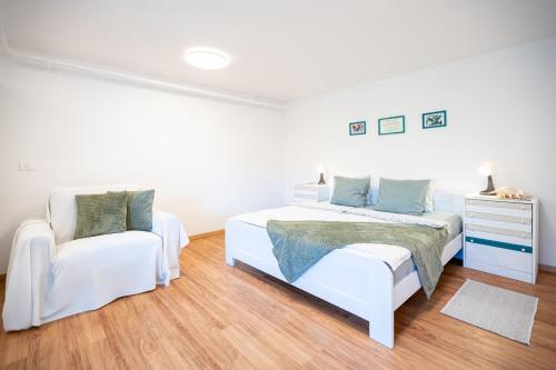 a white bedroom with a bed and a chair at Apartment Alba with garden in Piran