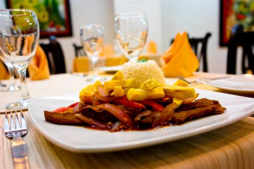 a white plate with food on a table with wine glasses at Intiotel Piura in Piura